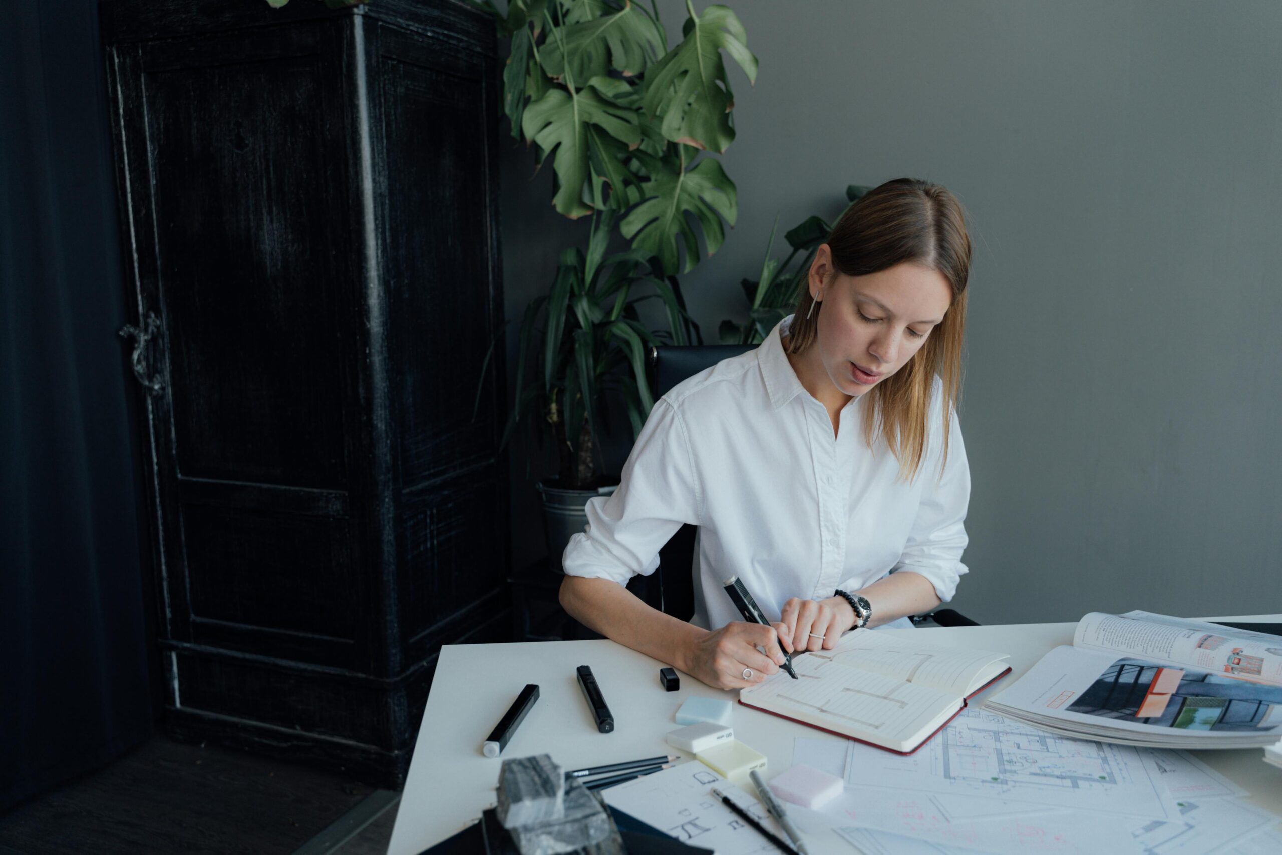 This is a photo of a landscape designer diligently working at a desk, surrounded by design materials. She is using Dubsado to streamline her landscaping business processes, enhancing productivity and organization.